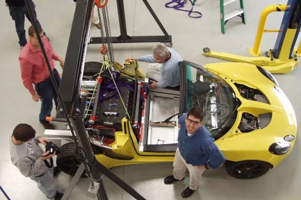 Early Tesla team working around a yellow development vehicle
